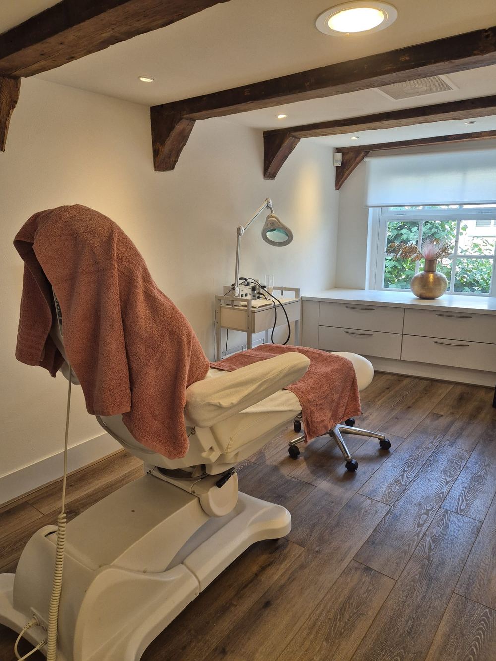 De behandelkamer van Feet & Body Wellness in Hoorn: een witte behandelstoel onder eeuwenoude houten balken, bij het raam